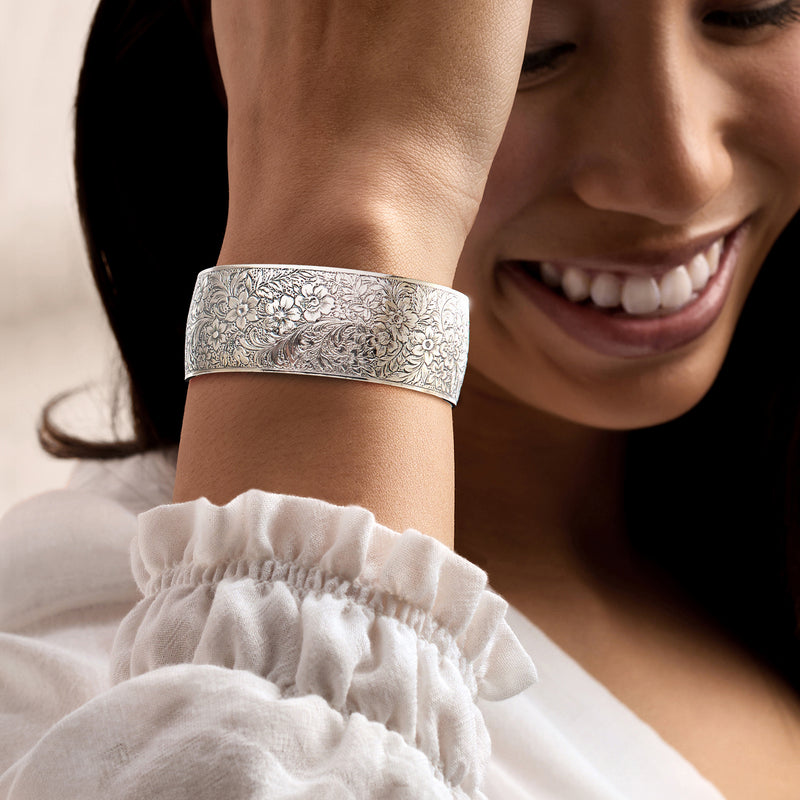 Wide sterling silver cuff bracelet with engraved floral pattern, worn on wrist