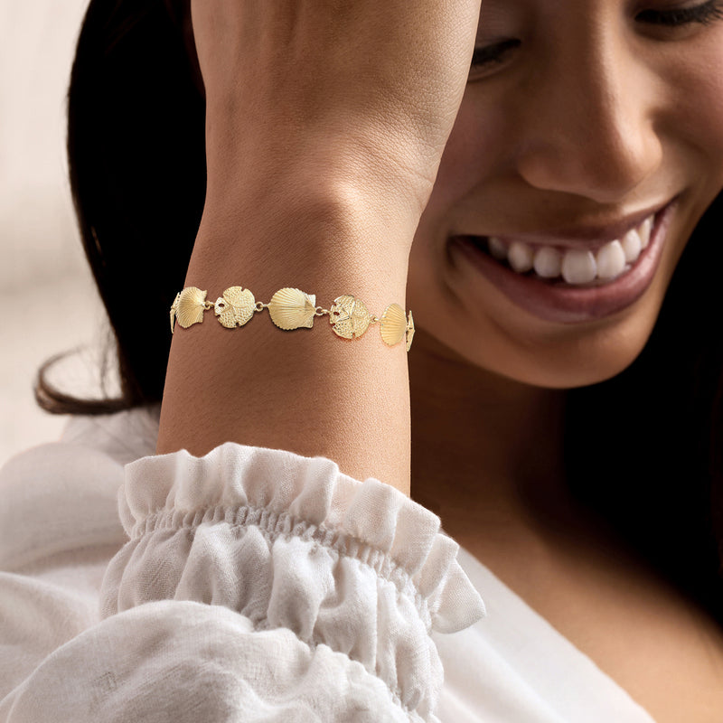 14kt yellow gold seashell charm bracelet worn on wrist with small toggle clasp