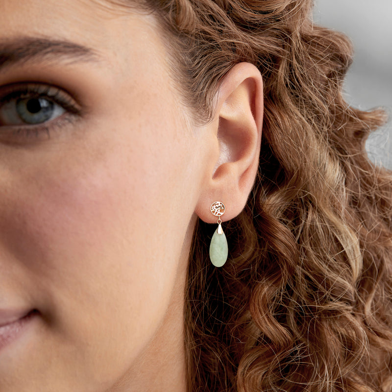 Gold drop earrings on ear with jade teardrop dangle and round symbol cap