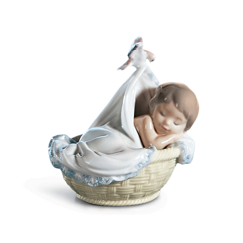 Porcelain figurine of a sleeping baby in a basket, white dress with blue detailing