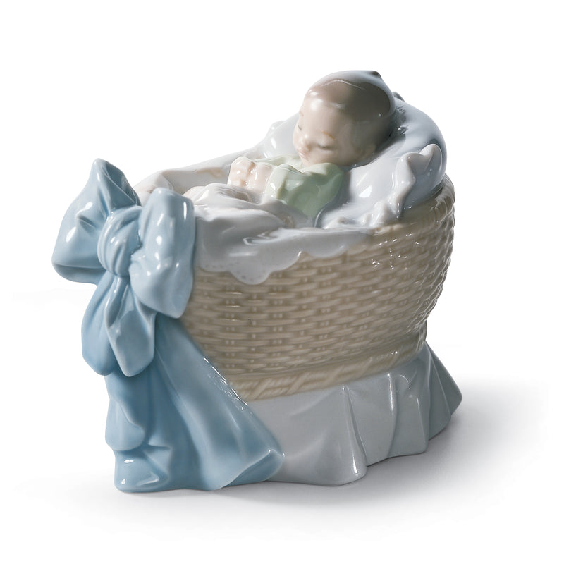 Lladro porcelain figurine of a boy in a cradle basket, blue and white wrapped blanket