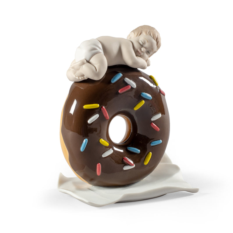 Porcelain baby figurine in a chocolate donut with colorful sprinkles, sitting pose