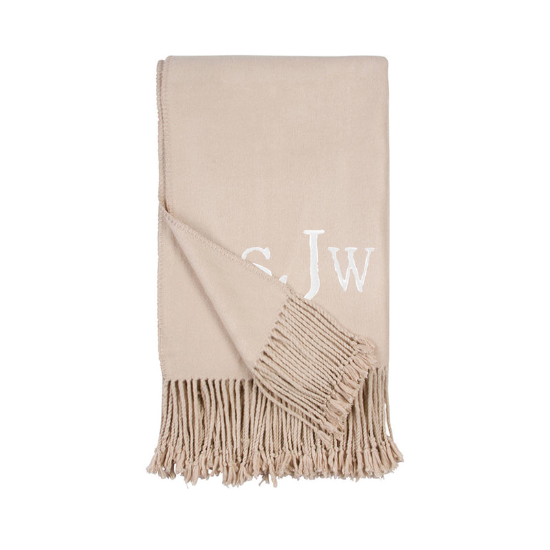 Beige throw blanket with white monogram and short fringe along the edge