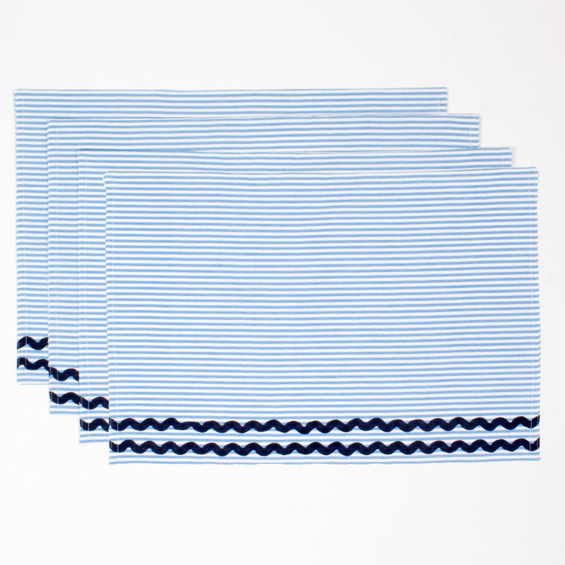 Set of four blue seersucker placemats with white stripes and dark zigzag trim