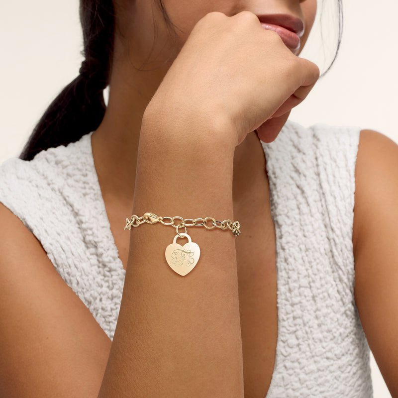 14kt yellow gold heart charm bracelet worn, featuring an engraved heart pendant
