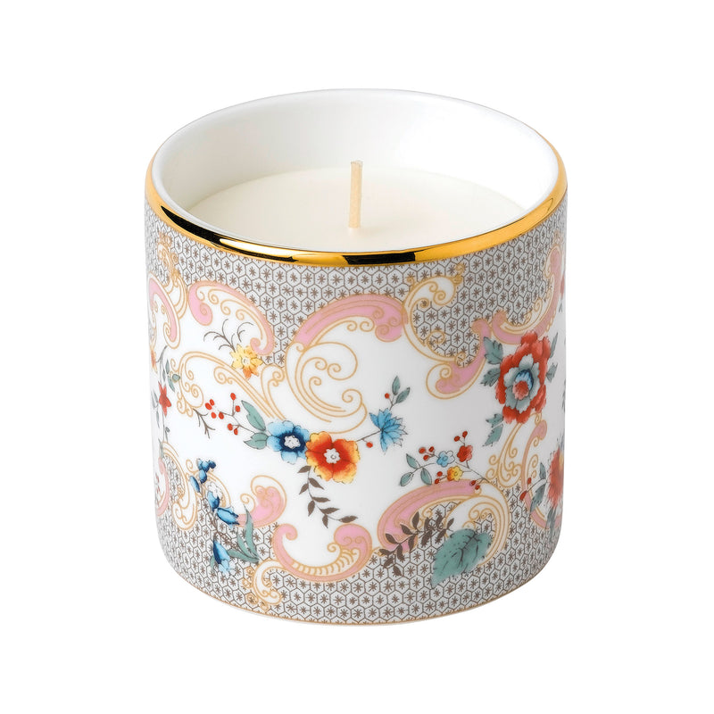 Floral rococo scented candle in ornate ceramic jar with gold rim and lit wick