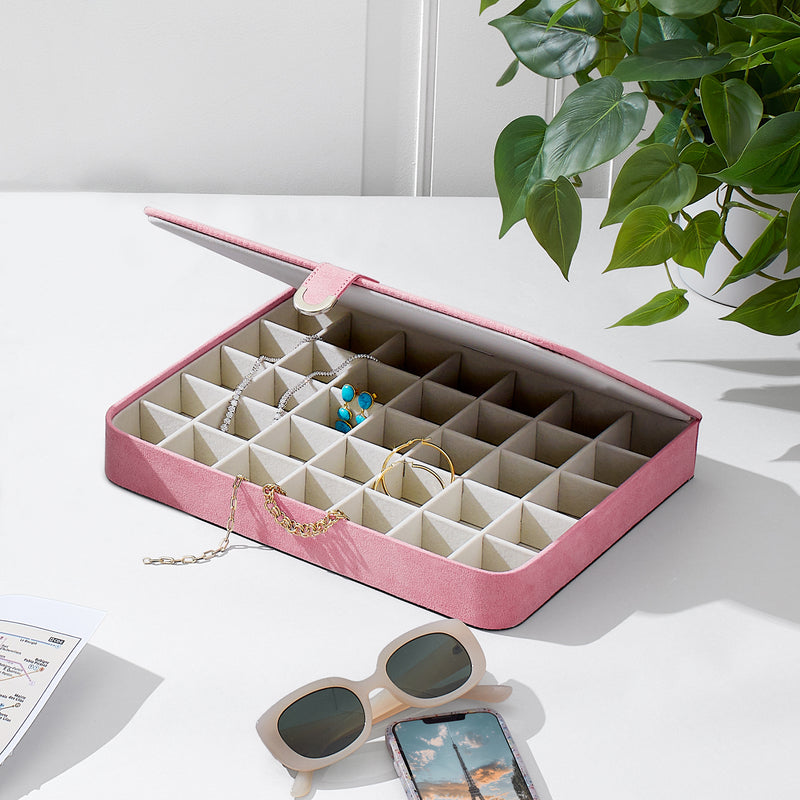 Pink jewelry case open with beige compartments and necklaces laid across the slots