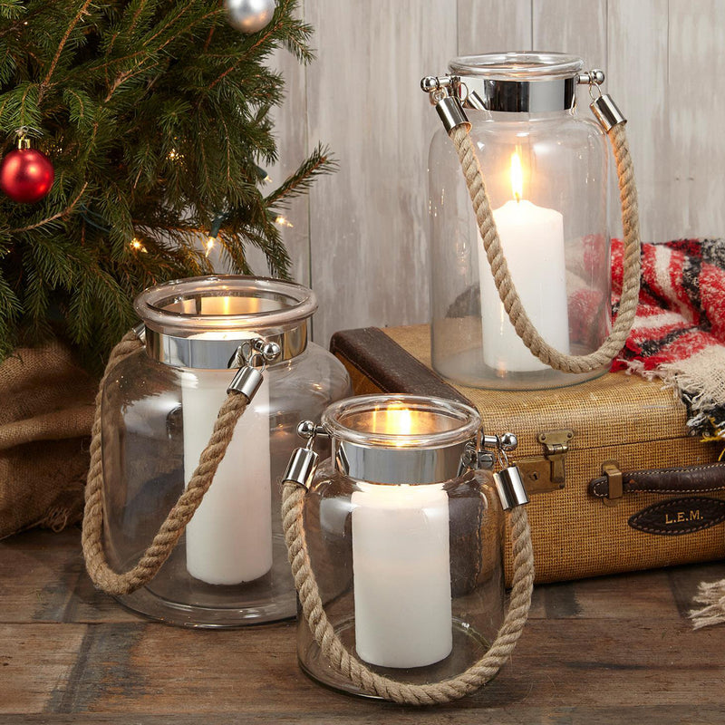 Set of three clear glass lanterns with metal tops and rope handles, warm candle light