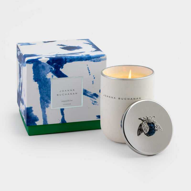 Sapphire scented candle in white jar with silver lid featuring blue gemstone emblem, with flame