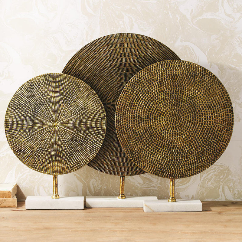 Set of three textured gold metal disc sculptures on white marble bases