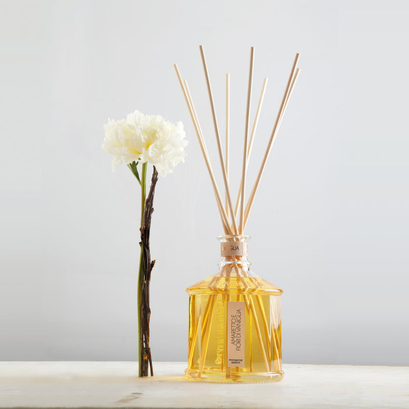 Erbario Toscano glass reed diffuser with amber liquid and light wood reeds, with flowers