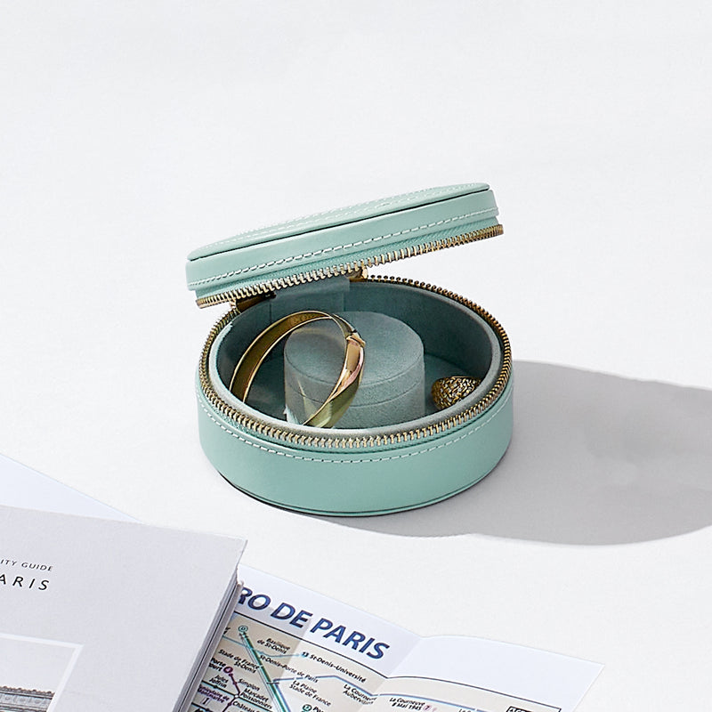 Jade green mini leather jewelry case open with ring compartment and gold zipper, small strap visible.