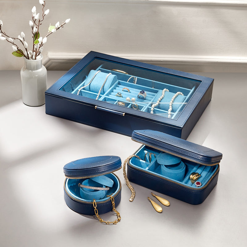 Indigo leather jewelry box open with window, displaying necklaces and rings, plus zip pouches