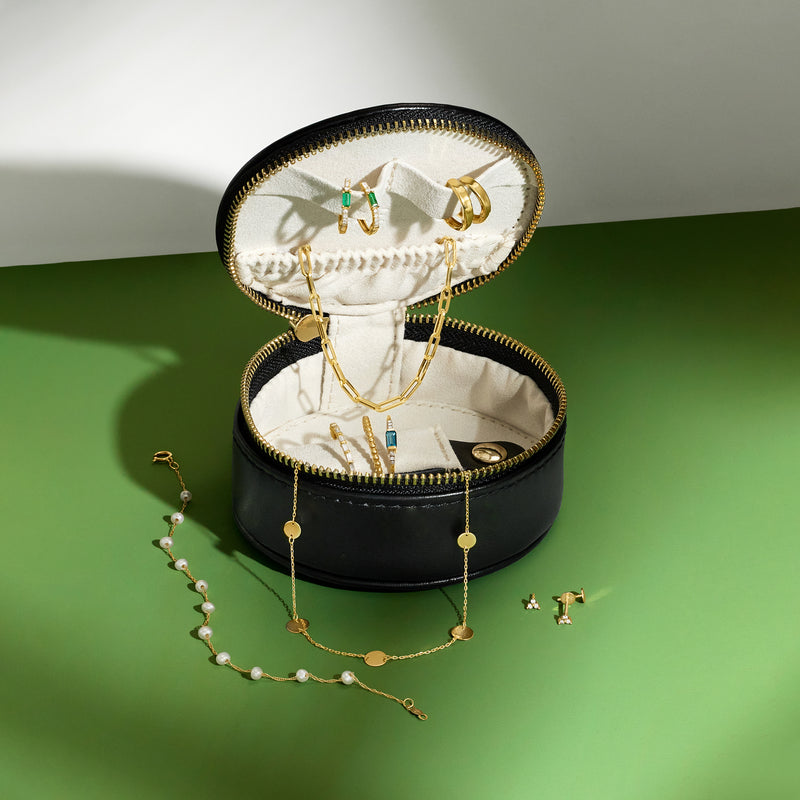 Black round travel jewelry box open, cream interior lining, gold chain and earring posts shown