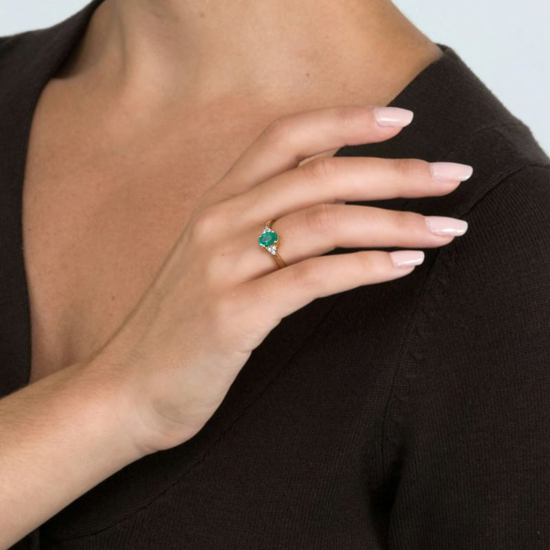 14kt yellow gold emerald ring on hand with oval green stone and diamond side stones