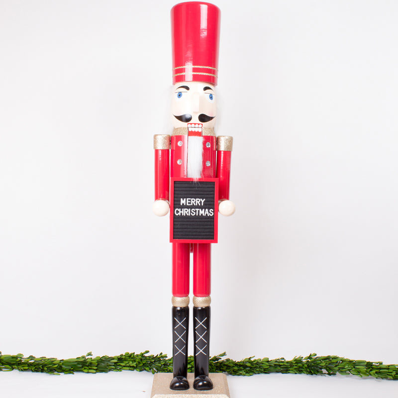Red nutcracker figure holding a Merry Christmas message board