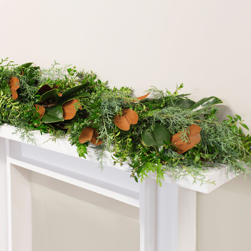 Fresh bunches garland with dense green foliage and orange leaf accents, draped across top