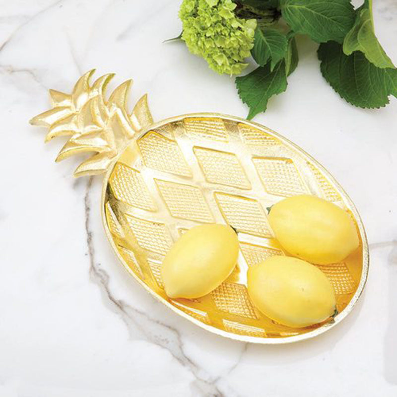 Gold metal pineapple-shaped serving tray with textured pattern, holding yellow pineapple slices.