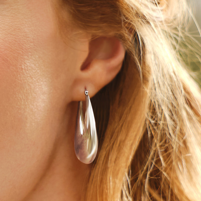 Sterling silver graduated hoop earrings on ear, glossy curved hoops, small clasp