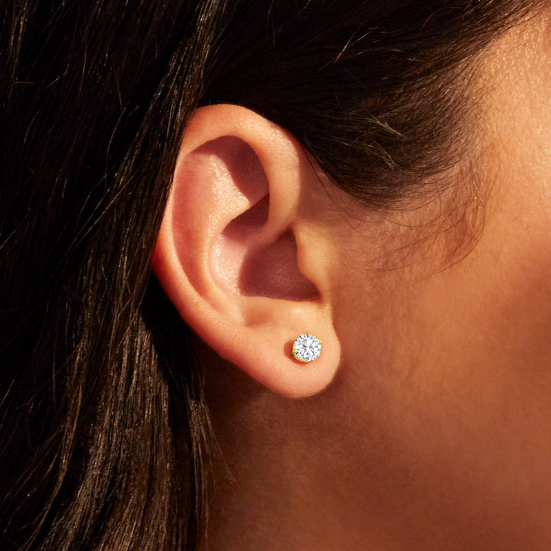 Round diamond stud earring in 14kt yellow gold on ear, close-up