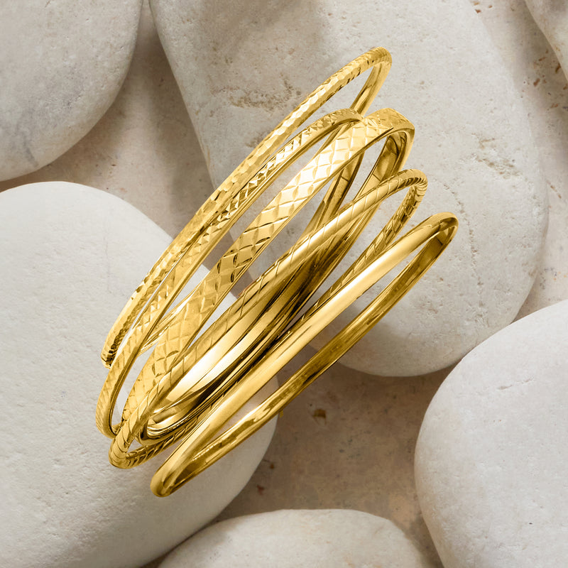 Five stacked gold bangles with diamond and dot textures, polished centers