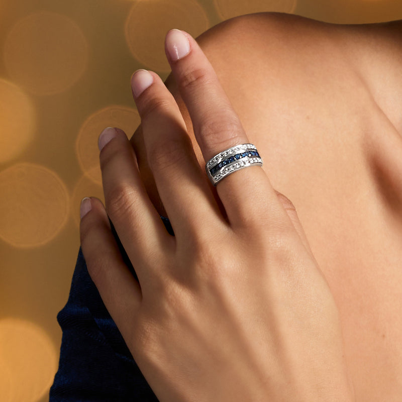 Sterling silver multi-row ring on finger with blue sapphire band and white topaz trim
