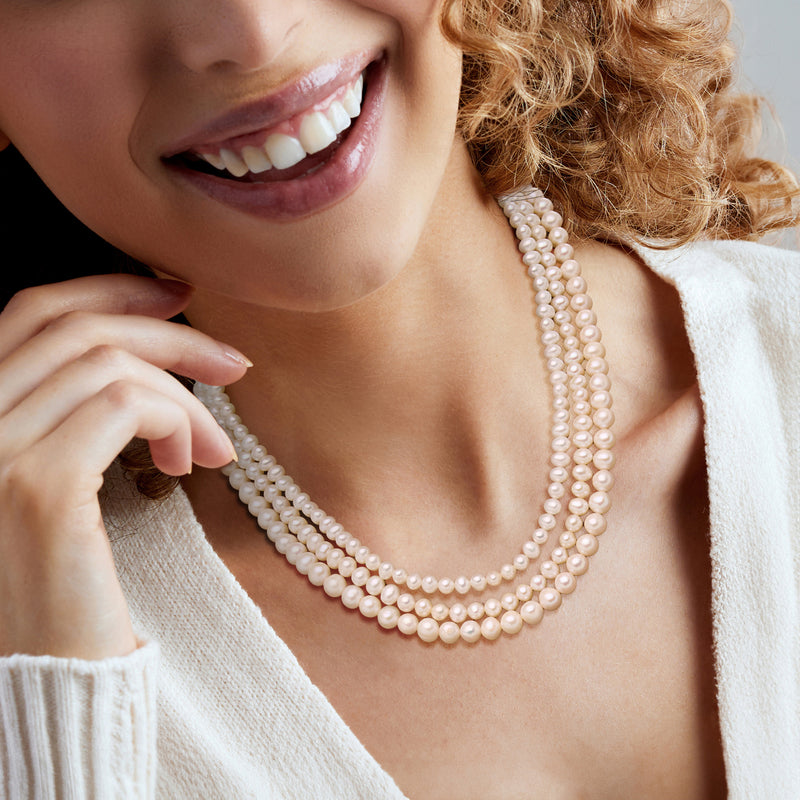 Cultured pearl three-strand necklace worn on neckline, round white pearls