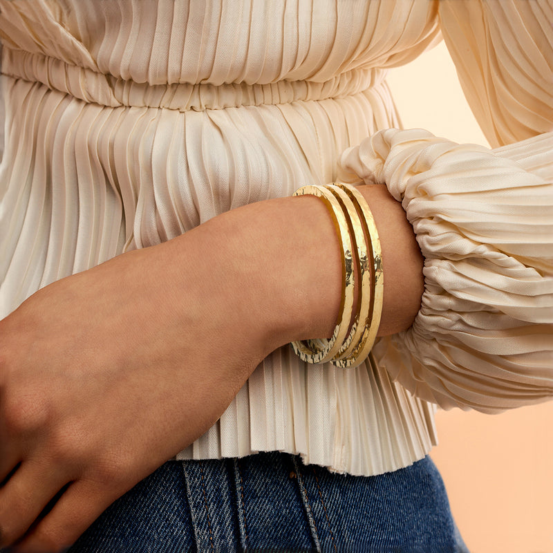 Three hammered gold bangle bracelets worn on wrist