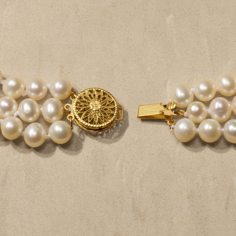 14kt yellow gold clasp with textured round center on graduated three-strand white pearls