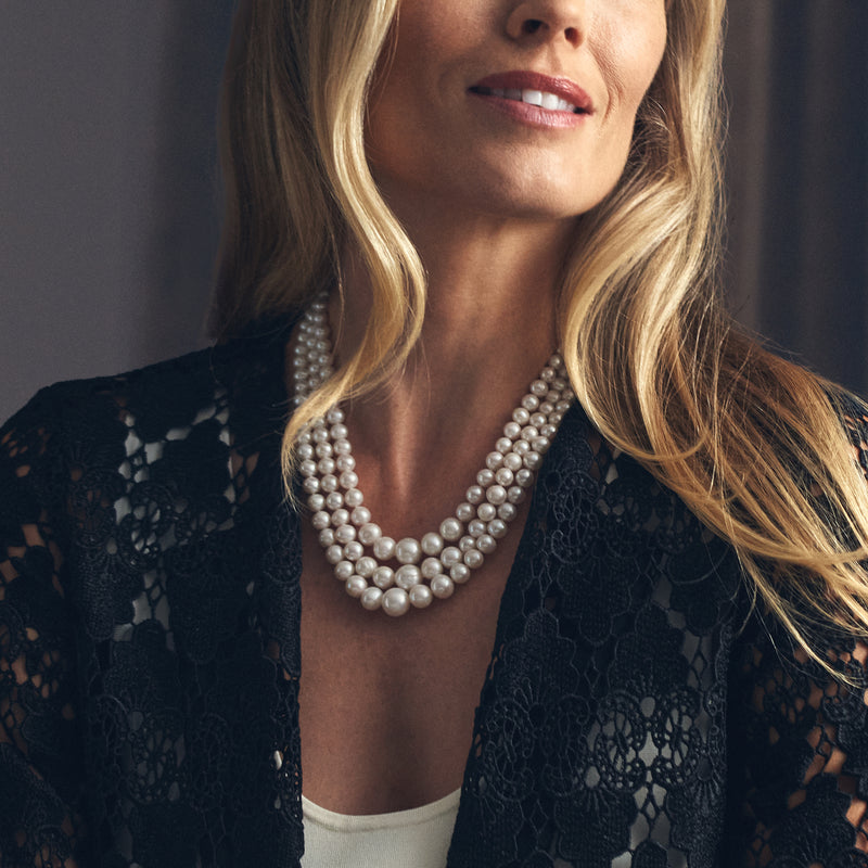 Cultured pearl three-strand necklace worn on neckline with white pearls and gold clasp