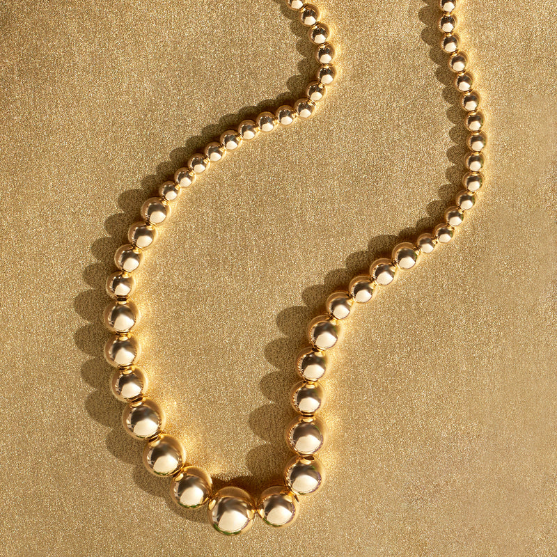 Graduated gold-tone bead necklace detail with glossy round links