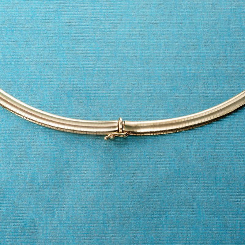 Close-up of 14kt yellow gold omega necklace clasp on blue fabric