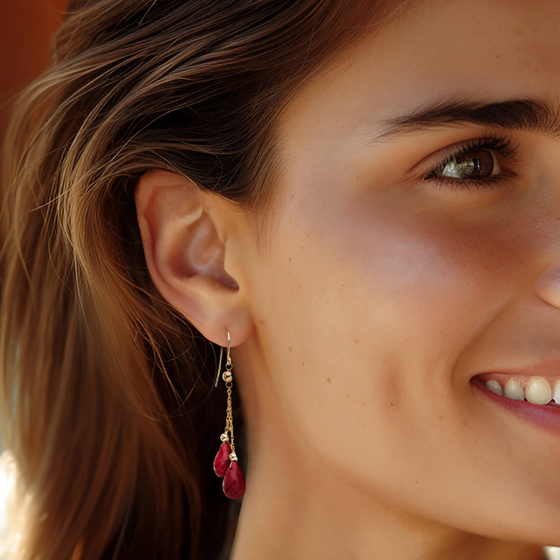Ruby-red teardrop drop earrings on yellow gold earwires, worn by a model