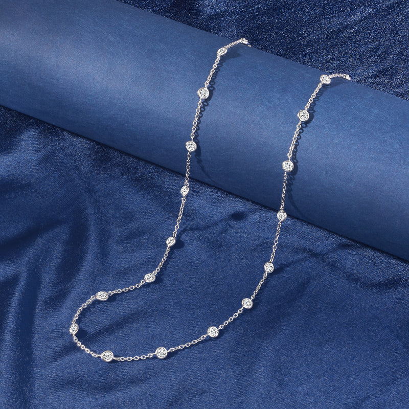 Sterling silver CZ station necklace with round bezel-set stones, flat lay