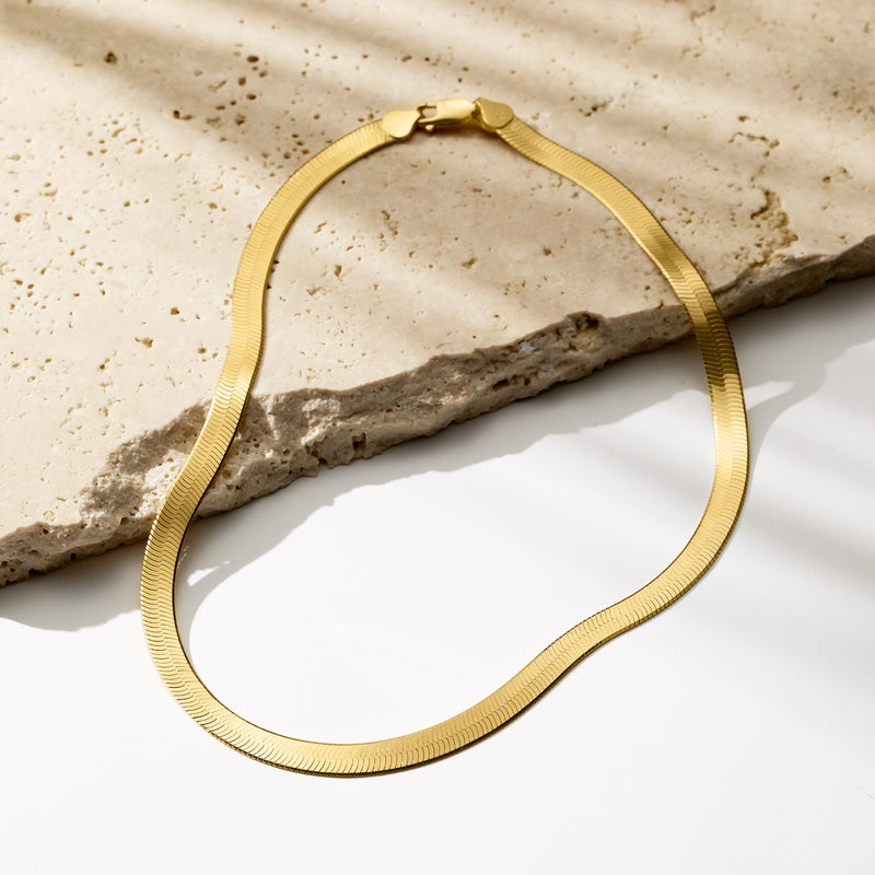 Gold herringbone necklace laid flat with clasp and curved chain shape