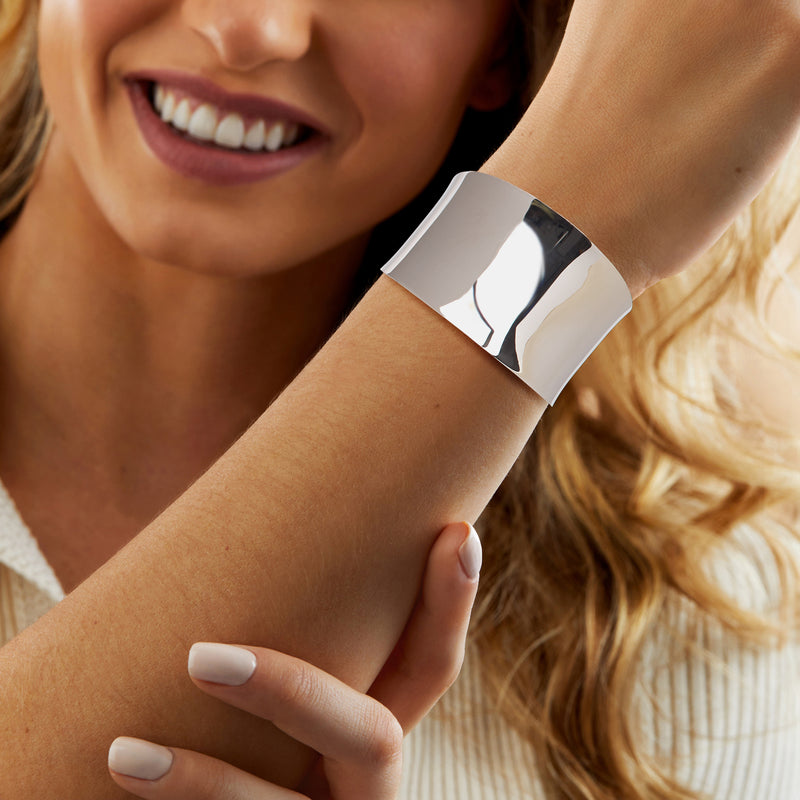 Wide polished silver cuff bracelet worn on wrist, open bangle style