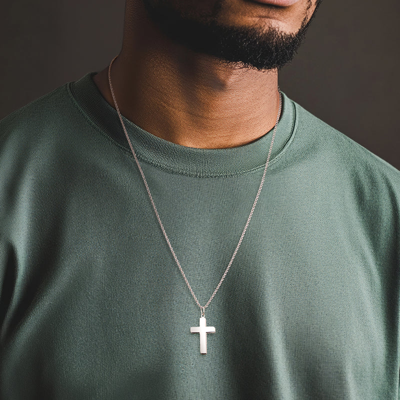 Sterling silver cross pendant necklace worn on a man’s chest, link chain visible