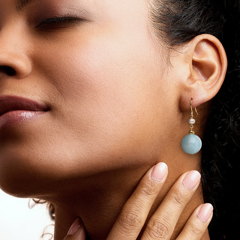Gold drop earrings with white pearl and round blue gemstone worn on ear