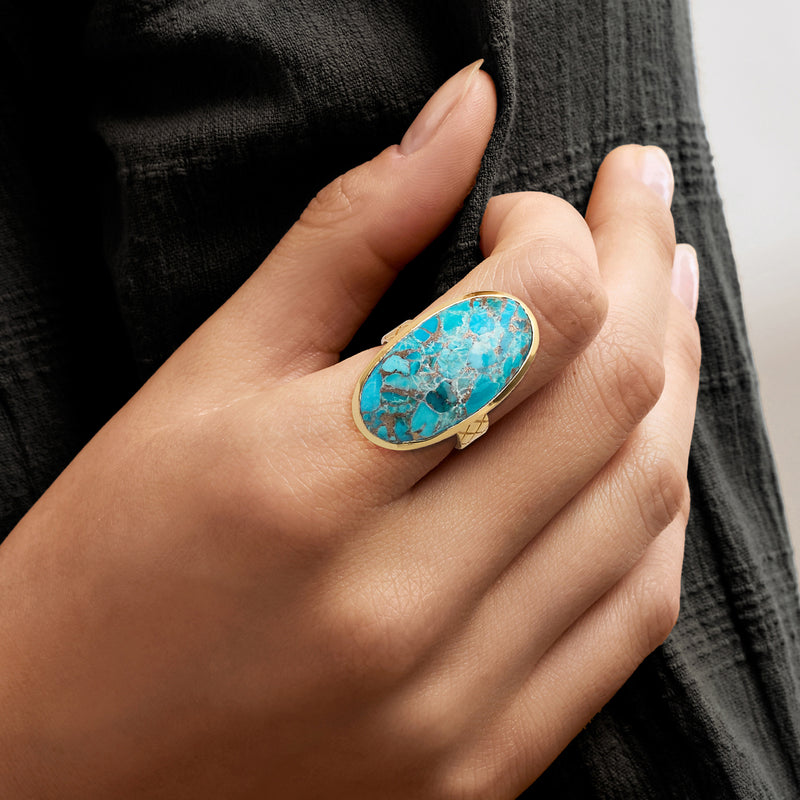 Turquoise oval ring in gold-toned setting worn on hand, silver-toned veining