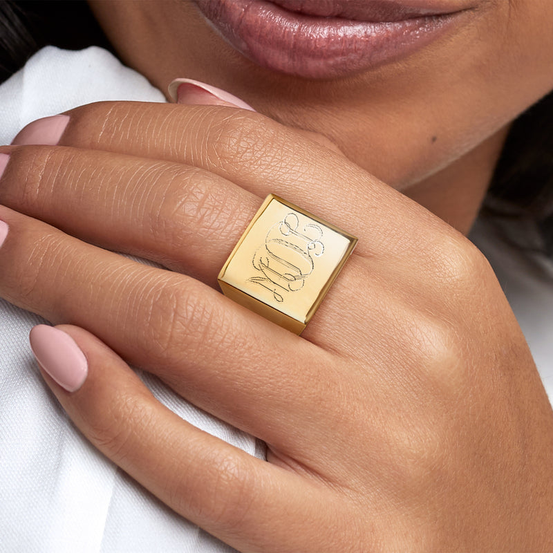Yellow gold square-top signet ring with engraved monogram on finger, close-up