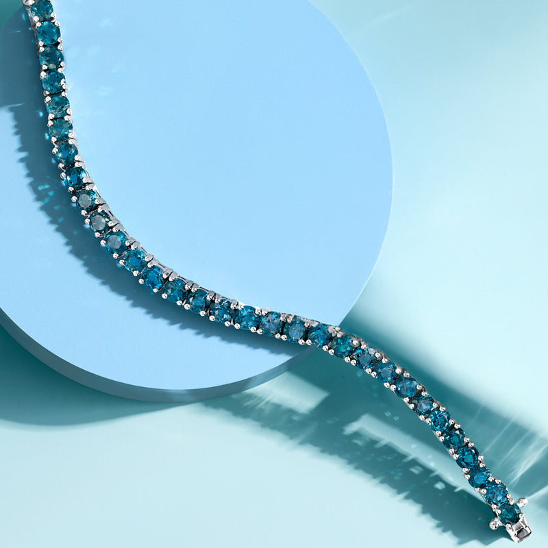 Close-up tennis bracelet with small blue topaz gemstones in silver prong settings