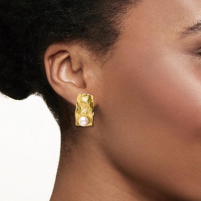 Gold sculptural cultured pearl earrings shown on ear, close-up