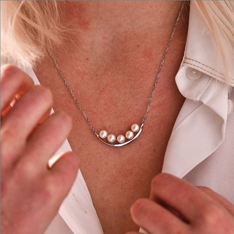 Sterling silver curved bar necklace with white cultured pearls, close-up on neck