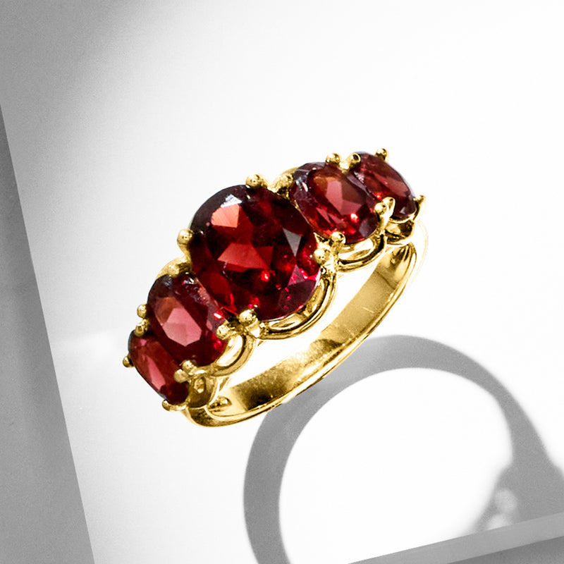 Five-stone garnet ring angled on hand with dark red gemstones and gold-tone band