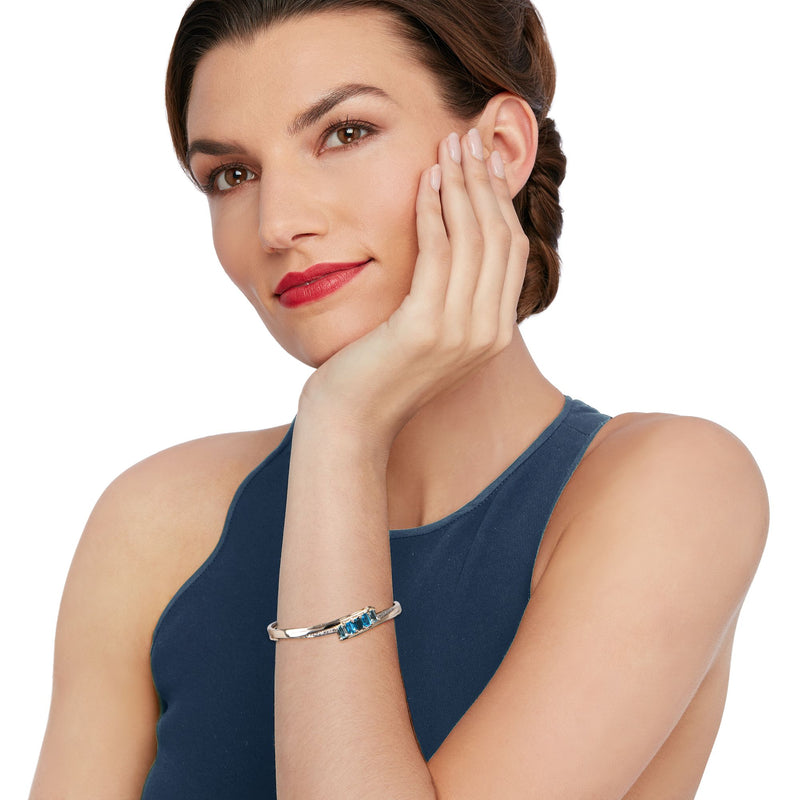 Gold bangle bracelet with rectangular blue topaz stone, worn on wrist