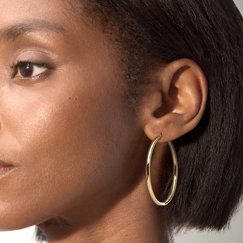 Model wearing yellow gold hoop earrings with smooth oval hoop profile