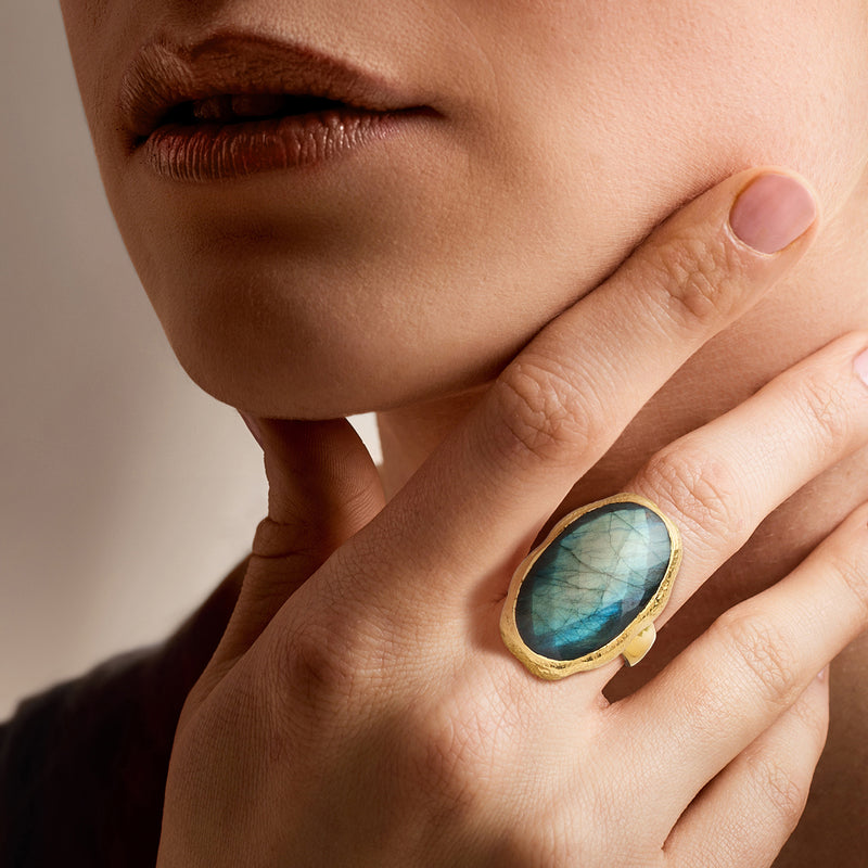 Labradorite oval ring on hand, blue-green iridescent stone in gold-tone bezel