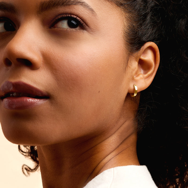 Huggie hoop earrings in 14kt yellow gold on ear, small polished oval hoops.