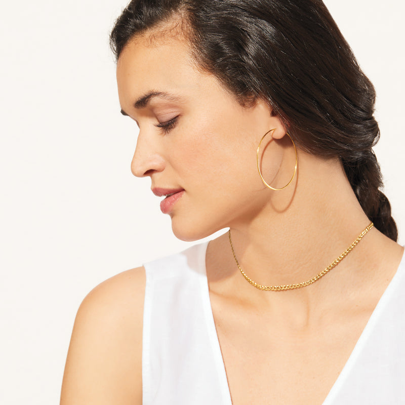 Yellow gold curb-link choker necklace worn at the base of the neck with a white top