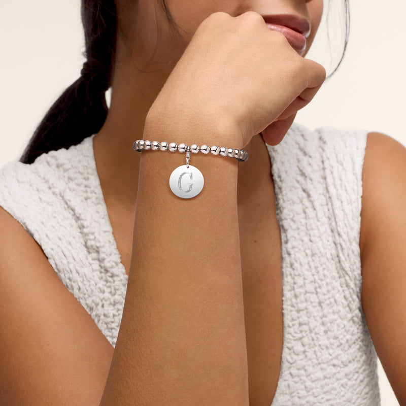 Sterling silver bead bracelet on wrist with round disc charm and letter G